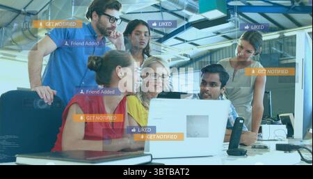Collaborating team viewing laptop screens in open-plan office, with social media notifications Stock Photo