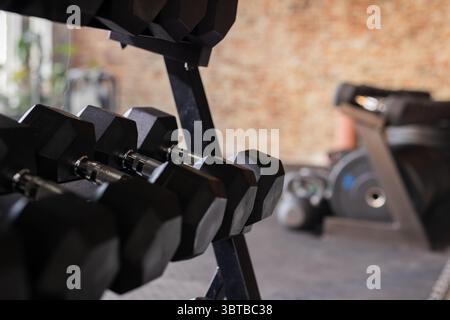 Black hexagonal dumbbells are resting on metal rack in gym near treadmill with natural light Stock Photo