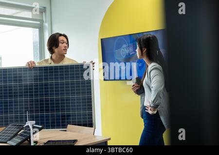 Asian coworkers holding solar panel while reviewing wind turbine model and screen in research lab Stock Photo