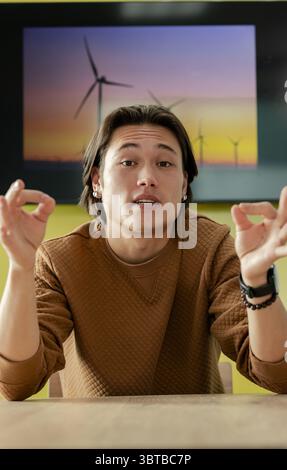 Asian man making OK gestures sitting at wooden table in room with wind turbine art Stock Photo