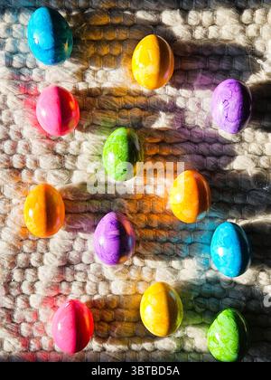 Brightly colored Easter eggs on textured wool rug in sunlight. Vibrant spring holiday backdrop. High quality photo Stock Photo