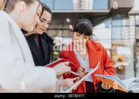 Three Professional Women Discussing Documents Outdoors in Modern Business District Stock Photo