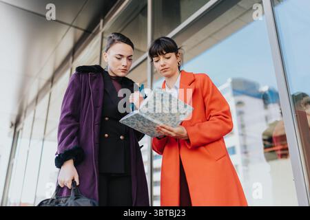 Two businesswomen collaborating outdoors while reviewing documents near a modern building. Stock Photo