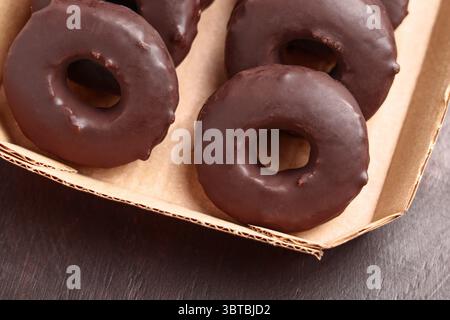 Chocolate donuts in cardboard pack on wooden table. Sweet baked dessert doughnuts. Close up. Stock Photo