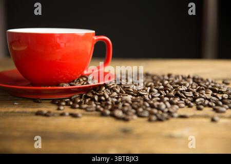 Flat design showing red coffee cup resting on wood table with scattered beans against dark backdrop Stock Photo