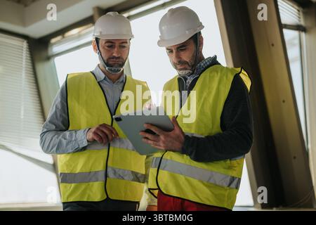 Two construction workers on-site discussing building plans using a digital tablet device Stock Photo