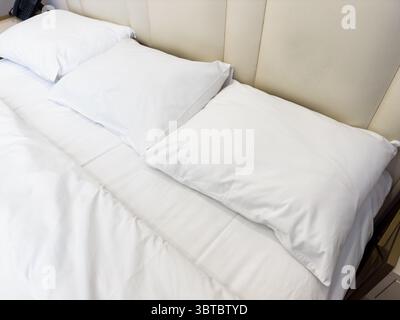 A white bed with three white pillows. The pillows are stacked on top of each other Stock Photo