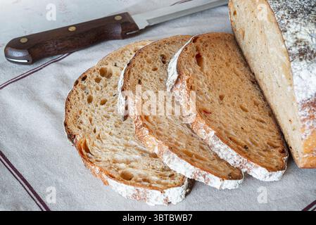 Slices of crusty artisanal bread rest on a linen cloth with a wooden knife beside them, showcasing the warmth of home baking. Stock Photo