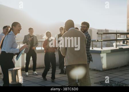 A joyful team of diverse business colleagues celebrates success with music and dance on a sunset-lit rooftop, creating a lively and motivating Stock Photo