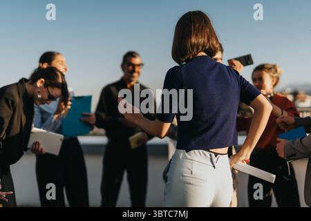 Diverse group of people takes a break to dance and enjoy music on a rooftop at sunset, promoting team bonding and joy in a relaxed atmosphere. Stock Photo