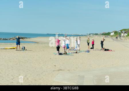 A group of people doing a yoga class and exercising on the beach uk Stock Photo
