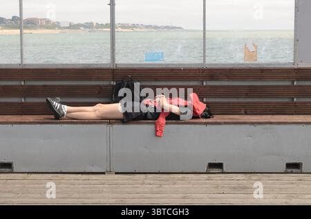 woman sleeping on a wooden bench on the pier on a hot summers day with her red jumper over her face to keep cool uk Stock Photo