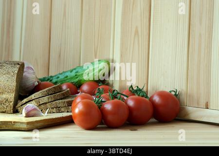 Fresh tomatoes, cucumbers, and bread laid out on a wooden cutting board. Stock Photo