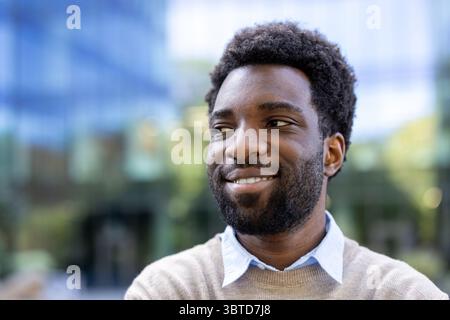 A smiling African American man looking off to the side, with a blurred building in the background. Stock Photo