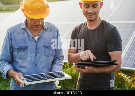 Engineers working at solar panels factory outdoor - Photovoltaic, renewable green energy and environmental concept - Main focus on tablet Stock Photo