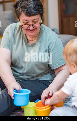 Grandmother playing with baby using colorful stacking cups on carpeted floor.  Stock Photo