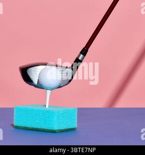 Golf club about to strike ball positioned on tee inserted in blue kitchen sponge Stock Photo