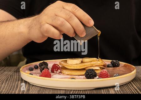 Close-up of a hearty breakfast scene with a stack of fluffy pancakes topped with fresh berries and syrup pouring, evoking cozy comfort and indulgence. Stock Photo