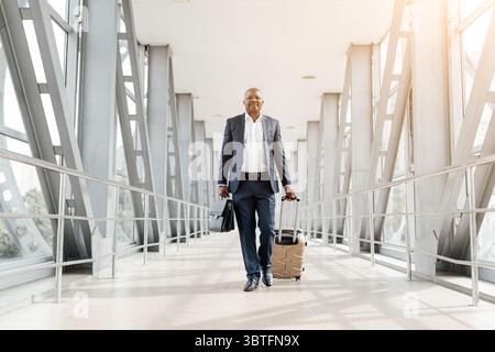 Businessman walking through airport pulling suitcase with relaxed but purposeful stride Stock Photo