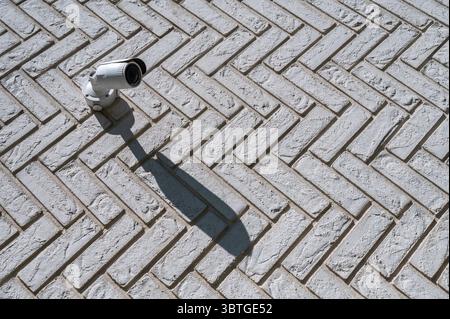 Security camera mounted on sunlit brick wall creates bold angular shadow. Scene highlights intersection of urban safety and architectural texture Stock Photo