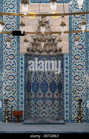 The ornate Mihrab of Rustem Pasha Mosque, decorated with intricate Iznik tiles and framed by elegant glass lamps under a high ceiling. Stock Photo