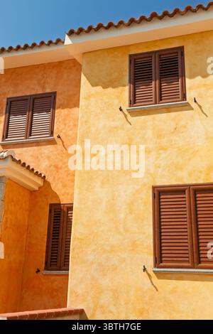 A sunlit Mediterranean-style building features vivid yellow and orange stucco walls with wooden shutters and a tiled roof, typical of southern Italian Stock Photo