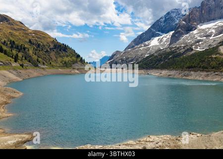 The serene turquoise waters of Lake Fedaia, nestled in the Dolomites, surrounded by towering mountains with snow-capped peaks and lush green slopes un Stock Photo