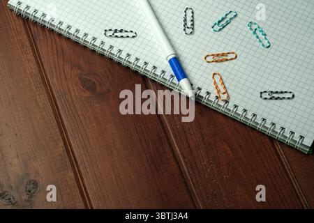 A collection of notebooks and colorful paperclips arranged on a wooden desk. Stock Photo
