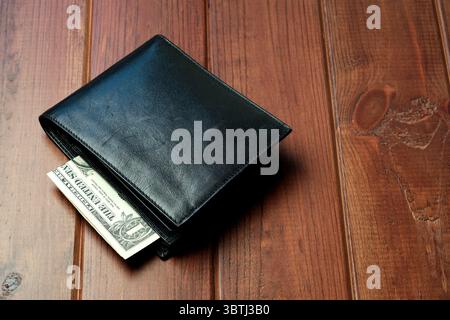A sleek black wallet sits on a rustic wooden table, partially opened with cash visible. Stock Photo