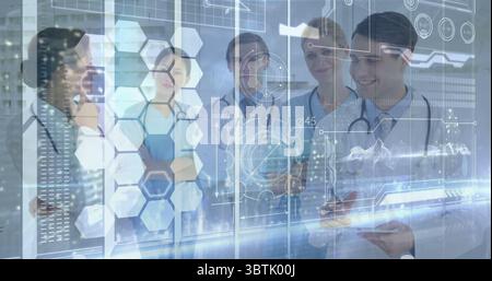 Gathering medical team examining digital interface on glass panel in hospital, with tablet computer Stock Photo