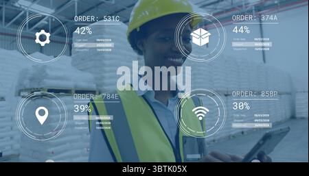 Monitoring woman in safety vest hard-hat using tablet in warehouse by stacks, with virtual overlays Stock Photo