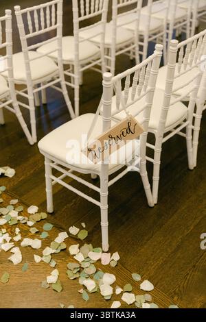 Chairs are arranged for a wedding, marked as reserved with petals scattered on the floor around them. Stock Photo