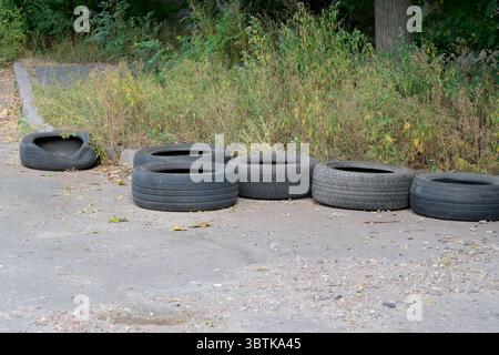 Old car tires on the side of a battered road with potholes, city photography in summer on a sunny day close-up Stock Photo