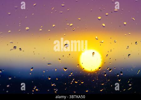 A vivid sunset glows in the background as raindrops cling to a window, capturing the contrast of warm light and cool colors after a rainfall Stock Photo