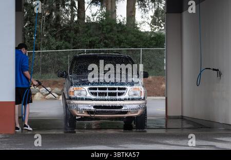 Man cleaning his car using high pressure water. Young man washing his car in a self-service car wash station. Professional car detailing and cleaning Stock Photo