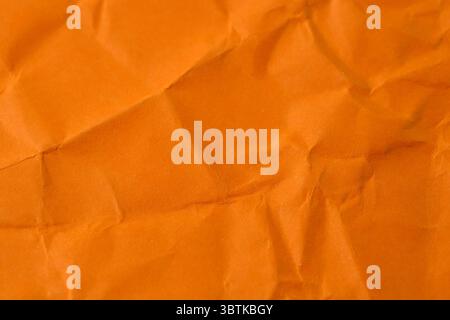A sheet of crumpled orange paper lies on the table, abstract stationery background, macro Stock Photo