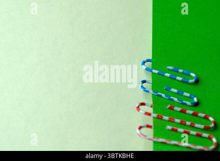 Red and blue paper clips on green blank sheets, stationery art background, close-up Stock Photo