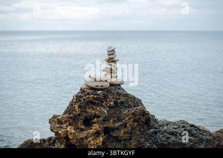 A stack of smooth stones balanced on a rocky surface by the sea. Stock Photo