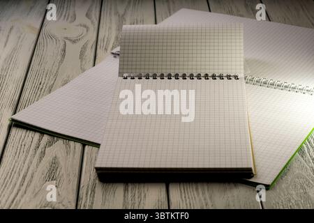 Opened blank notebooks with checkered tear-off leaves on a wooden table in the twilight light stationery educational background Stock Photo