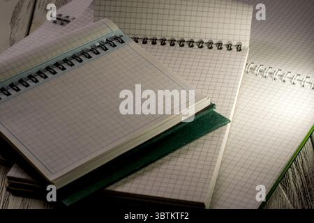 Opened blank notebooks with checkered tear-off leaves on a wooden table in the twilight light stationery educational background Stock Photo