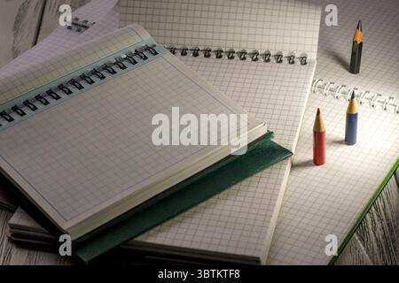 Opened blank notepads with checkered loose-leaf papers with pencils in twilight light stationery educational background Stock Photo
