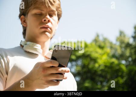 Young caucasian man listen music and holding mobile phone in nature summer background. Check apps, focused on device, chatting or browsing internet. O Stock Photo
