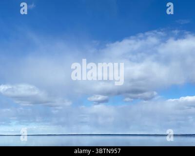 The vast blue sky is filled with soft white clouds, reflected in the calm water below. Stock Photo