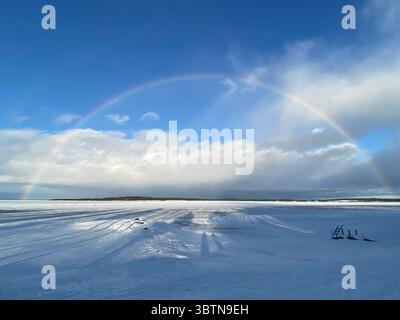 A stunning rainbow appears over a snow-covered field on a bright winter day. Stock Photo