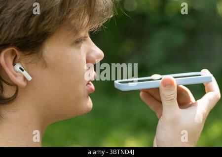 Young caucasian blond man recording voice message on cellphone. Man using virtual voice assistant. Outdoors. Close up Stock Photo