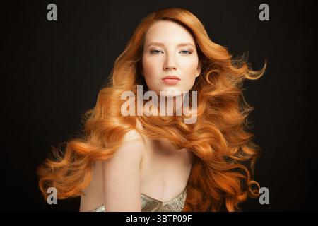 Portrait of beautiful young redhead woman with curly, long hair against black background Stock Photo
