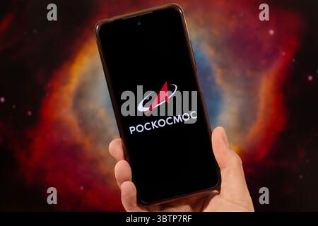 BOGOTA, COLOMBIA - JULY 14 OF 2025 A male hand holding a smartphone with his right hand and Roscosmos logo in russian with blurred nebula at backgroun Stock Photo