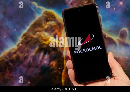 BOGOTA, COLOMBIA - JULY 14 OF 2025 A male hand holding a smartphone with his right hand and Roscosmos logo in russian with blurred space image at back Stock Photo