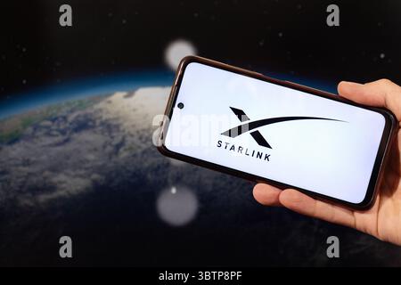 BOGOTA, COLOMBIA - JULY 14 OF 2025 A male hand holding a smartphone with Starlink logo and a blurred planet earth in space at background Stock Photo