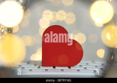 Online dating site. Wooden heart on computer keyboard against blurred lights, view through magnifying glass. Bokeh effect Stock Photo